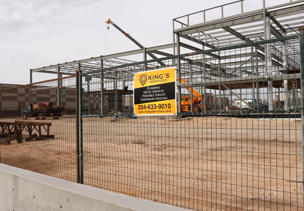 Construction site with steel frame building, yellow warning sign, and fenced perimeter