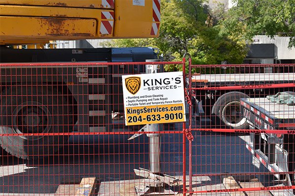 Construction site with red fence, heavy machinery, and King’s towing sign with phone number 204-633-9010