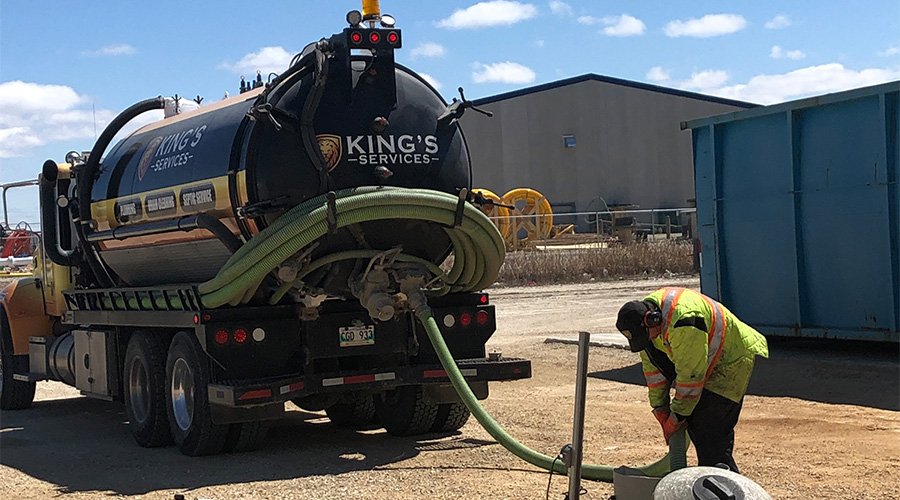A worker connects a green hose to a black septic truck labeled