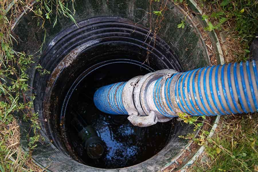 Blue hose inserted into a round underground manhole with standing water.